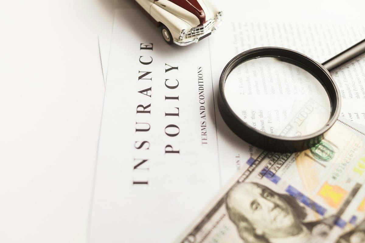 A magnifying glass resting on a printed insurance policy beside a pen and banknotes.